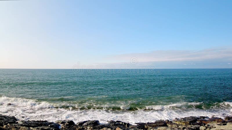 Vue statique en temps réel des vagues s'écrasent sur des rochers sur la plage avec un horizon banque de vidéos