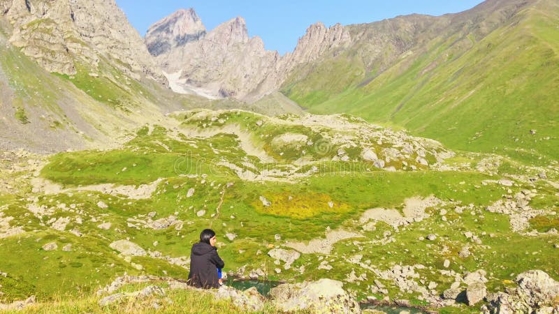 Vue statique femme réfléchie assis sur une falaise rocheuse avec panorama de montagnes pittoresques banque de vidéos