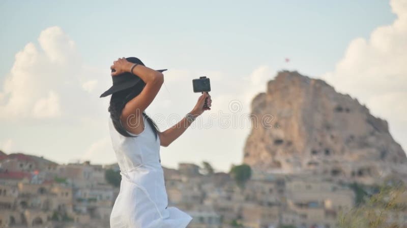 Vue statique jeune femme touriste en robe blanche avec smartphone sur trépied panoramique et capture vacances clips vidéos