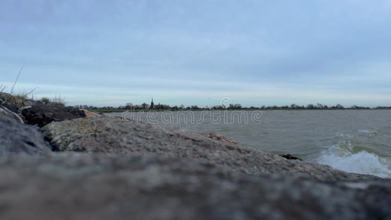 Vue statique sur un lac avec des vagues calmes qui s'éclaboussent sur les rochers clips vidéos