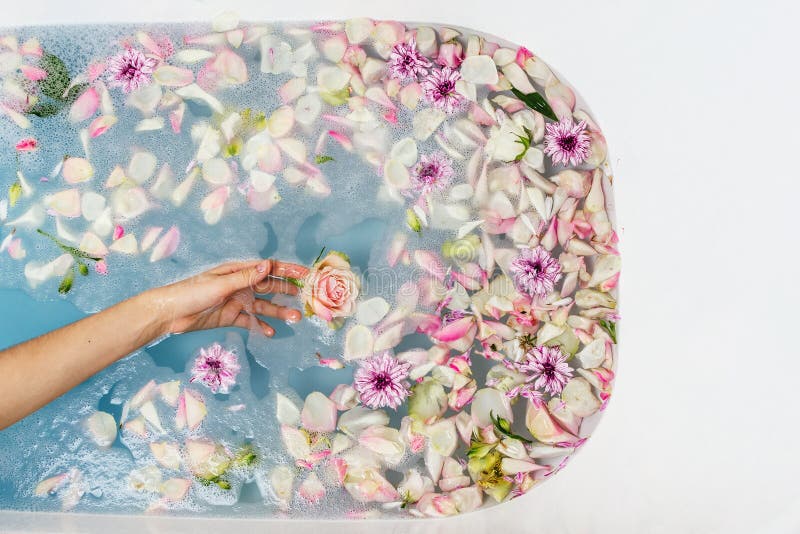 Vue supérieure de bain remplie d'eau, de fleurs et de pétales bleus de bulle avec la main de la femme images libres de droits Vue supérieure de bain remplie d'eau, de fleurs et de pétales bleus de bulle avec la main de la femme images libres de droits