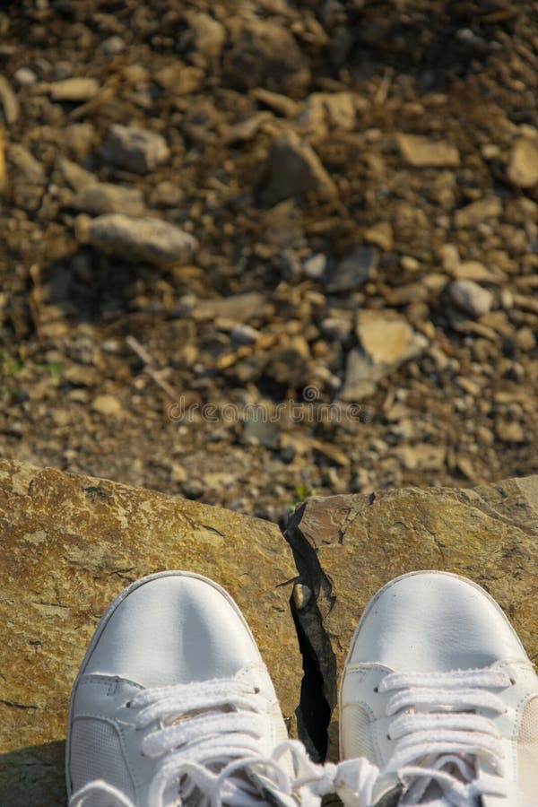 Vue supérieure des espadrilles blanches sur une roche de montagne photographie stock Vue supérieure des espadrilles blanches sur une roche de montagne photographie stock