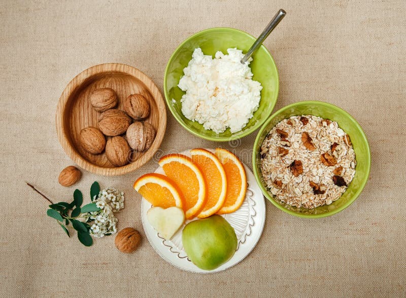 Table Appointments for Healthy Organic Breakfast.Walnuts,Oatmeal and Cottage Cheese.Cut Orange and Apple.Green Ceramic and Wooden Plates with Flowers. Table Appointments for Healthy Organic Breakfast.Walnuts,Oatmeal and Cottage Cheese.Cut Orange and Apple.Green Ceramic and Wooden Plates with Flowers.