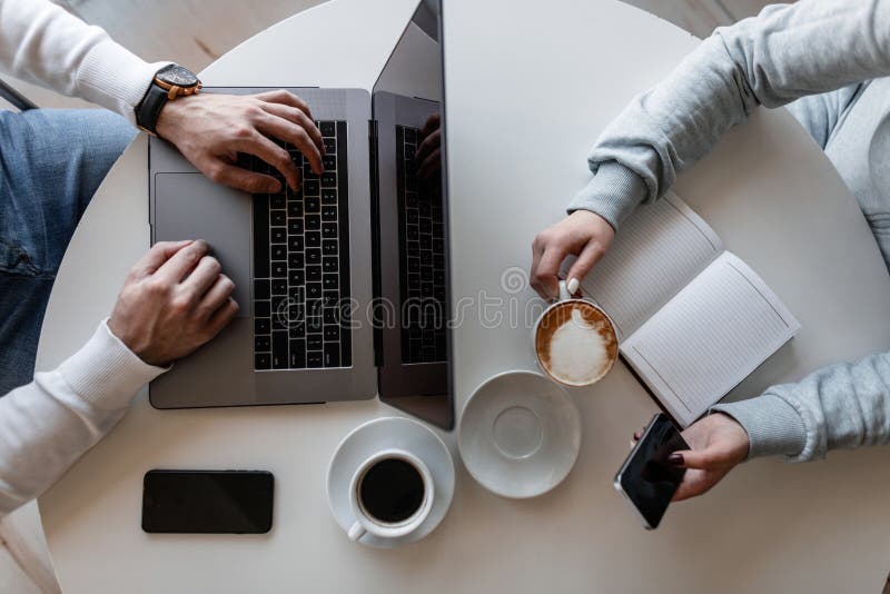 Vue supérieure sur une table blanche à laquelle repose un homme avec un ordinateur portable et une femme avec un bloc-notes avec photo stock Vue supérieure sur une table blanche à laquelle repose un homme avec un ordinateur portable et une femme avec un bloc-notes avec photo stock