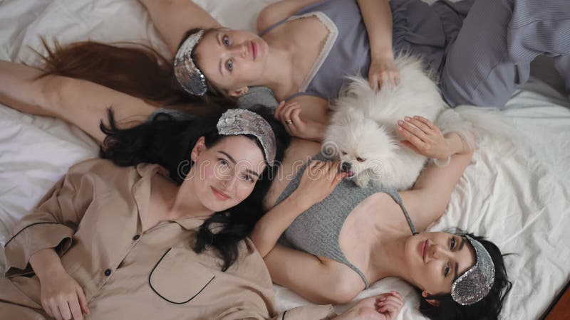 Vue supérieure. trois filles avec des masques de sommeil argentés sur la tête et un chien spitz blanc se couchent élégamment sur l