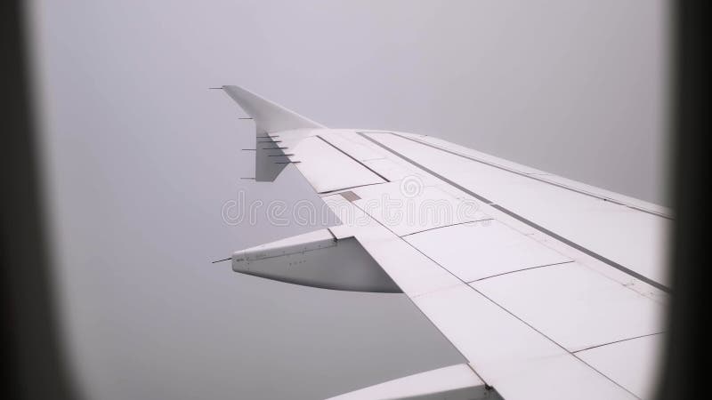 Vue sur une aile d'avion dans les nuages à travers un hublot. fond de ciel nuageux. un avion à passagers volant dans le brouillard banque de vidéos