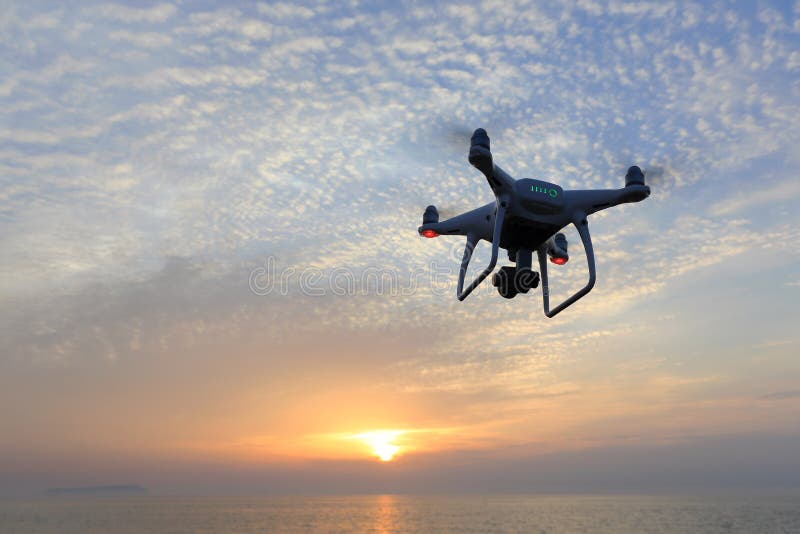 KAGAWA, JAPAN - APRIL 22, 2017: Remote controlled drone Dji Phantom4Pro equipped with high resolution video camera flying above the sea against a sunset sky. KAGAWA, JAPAN - APRIL 22, 2017: Remote controlled drone Dji Phantom4Pro equipped with high resolution video camera flying above the sea against a sunset sky.