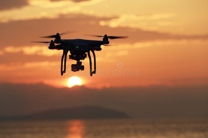 KAGAWA, JAPAN - JUNE 19, 2016: Remote controlled drone Dji Phantom 3 equipped with high resolution video camera flying above the beach against a sunset. KAGAWA, JAPAN - JUNE 19, 2016: Remote controlled drone Dji Phantom 3 equipped with high resolution video camera flying above the beach against a sunset.