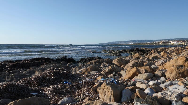 Vuil rotsachtig die strand met plastic flessen en document afval wordt gevuld Stapel van afval op het strand