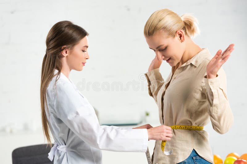 Vy över dietitisen i vit rock som mäter midjan för patienten arkivfoto