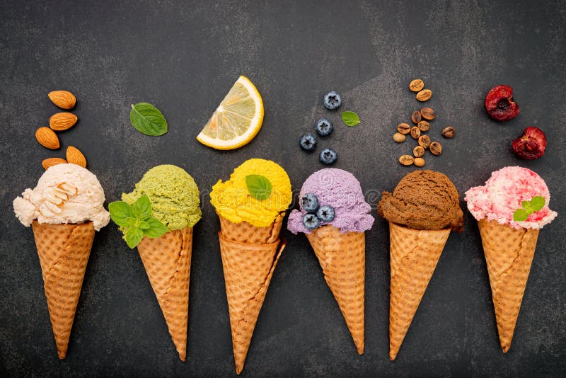 Vários sabores de gelado em cones blueberry green tea pistachio almond larange e cereja armada em fundo escuro de pedra .