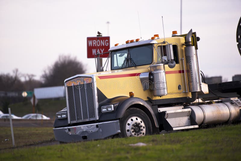 Large popular classic semi - truck with chrome accents on highway exit with sign wrong way. The truck is tilted forward in the plane of inclination of the road and lit by the rays of the setting sun. Large popular classic semi - truck with chrome accents on highway exit with sign wrong way. The truck is tilted forward in the plane of inclination of the road and lit by the rays of the setting sun.