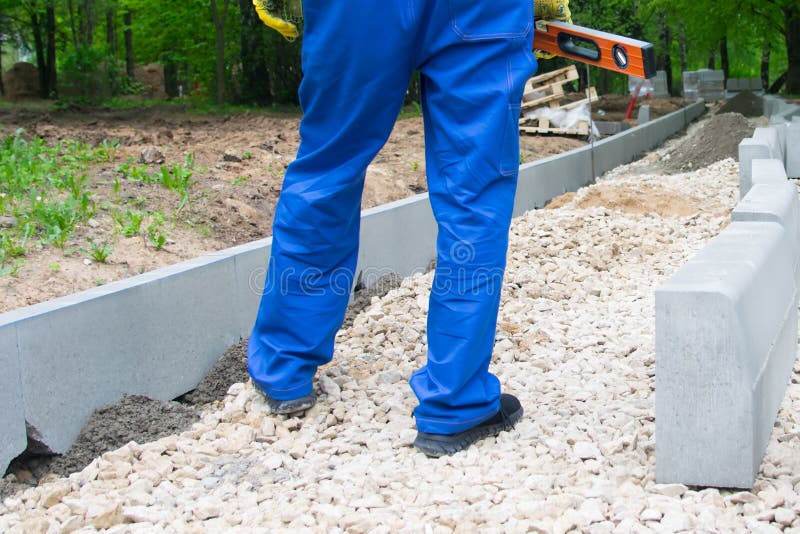 Vägkonstruktion och installation av trottoarkanter i parkerar, foten av arbetaren i blå likformig royaltyfria foton Vägkonstruktion och installation av trottoarkanter i parkerar, foten av arbetaren i blå likformig royaltyfria foton