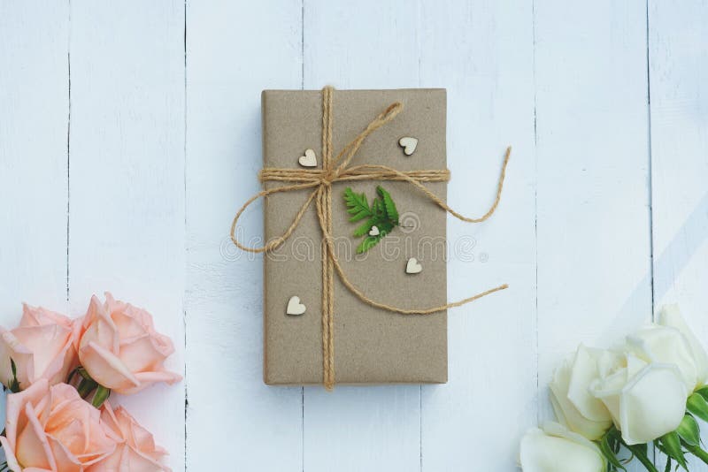 Vänlig gåvaask för brun eco som dekoreras med den mjuka rosa och vita rosen på den vita trätabellen, sött älskvärt närvarande val royaltyfri fotografi Vänlig gåvaask för brun eco som dekoreras med den mjuka rosa och vita rosen på den vita trätabellen, sött älskvärt närvarande val royaltyfri fotografi