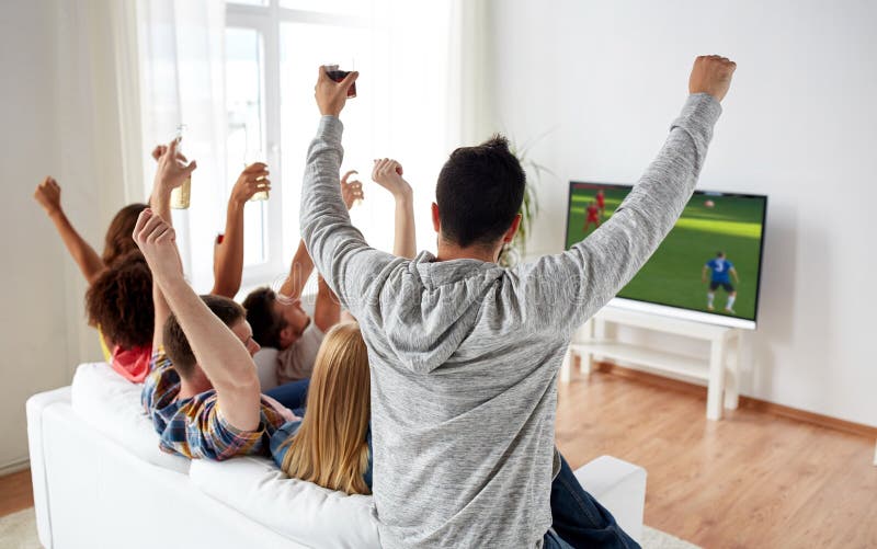 Vänner som håller ögonen på fotboll på tv och firar mål royaltyfri bild Vänner som håller ögonen på fotboll på tv och firar mål royaltyfri bild
