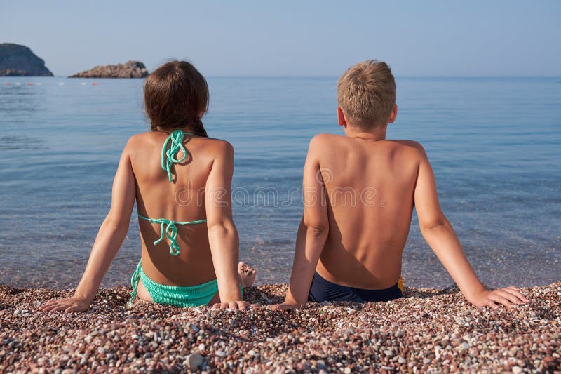 Vännpojke och flicka sitter på kusten och tittar på avståndet. sommarsemester på semester. Vännpojke och flickbror och syster sitter på kusten och tittar på avståndet. bakvy.