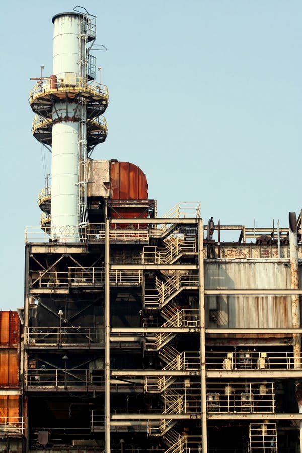 A power plant with levels of stairways and stacks in front of a clear blue sky. A power plant with levels of stairways and stacks in front of a clear blue sky