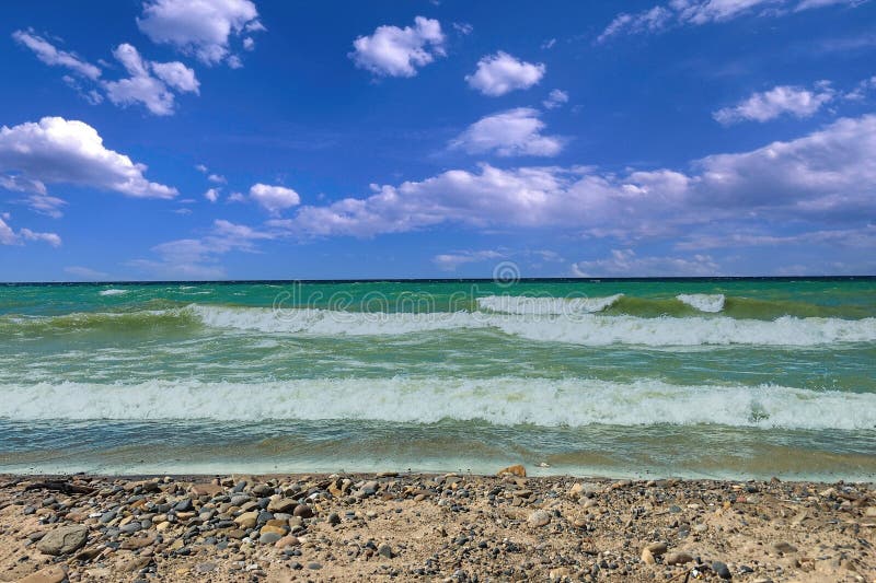 Waves crash ashore on a rocky beach under a blue sky with puffy clouds. Waves crash ashore on a rocky beach under a blue sky with puffy clouds.