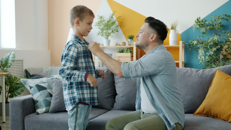 Vårdande pappa som hjälper liten pojke med klädesplagg som pratar inomhus hemma lager videofilmer