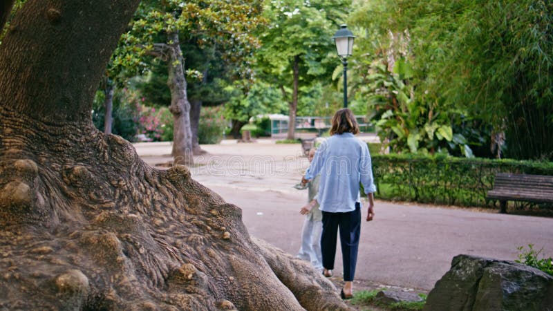 Vårdnadsmodern som ger hand till barnet i sommarparken. Lilla dotters hoppträd lager videofilmer