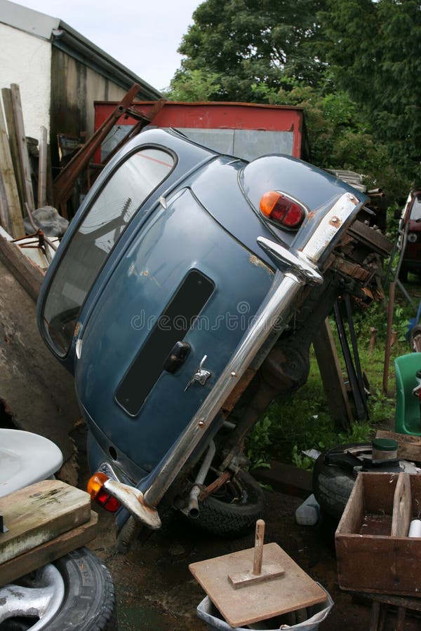 Old abandoned blue car on its side in a junkyard surrounded by scrap objects. Old abandoned blue car on its side in a junkyard surrounded by scrap objects.