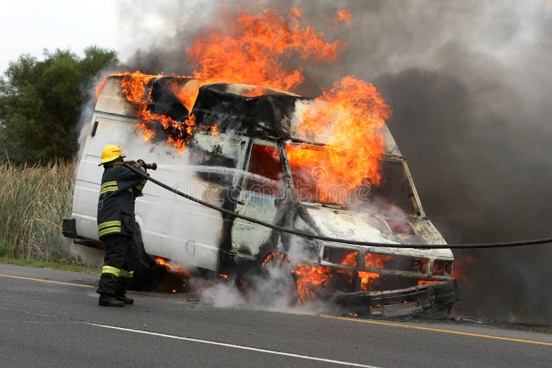 Fireman spraying water into a burning van on a road. Fireman spraying water into a burning van on a road