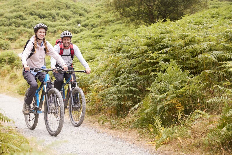 Vélos de montagne de monte de jeunes couples adultes dans la campagne, intégrale photo stock Vélos de montagne de monte de jeunes couples adultes dans la campagne, intégrale photo stock