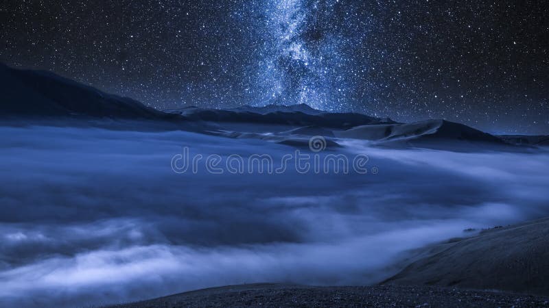 Vía láctea sobre las nubes que fluyen en las montañas en la noche, Italia de Castelluccio