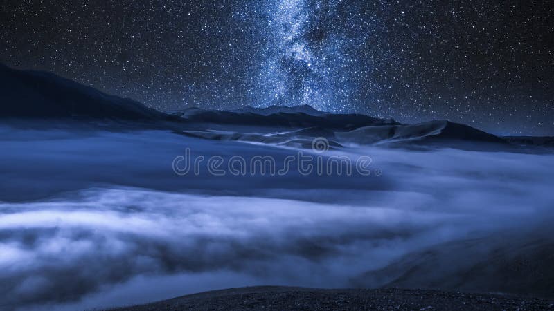 Vía láctea sobre las nubes que fluyen en las montañas en la noche, Italia de Castelluccio