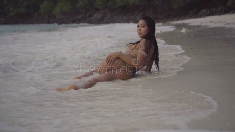 Vídeo de la muchacha atractiva que miente en la arena con salpicar el agua y el tacto sensual - de la visión trasera en la cámara almacen de metraje de vídeo