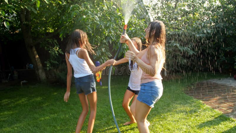 Vídeo de movimento lento dos adolescentes alegres que dançam e que saltam com a mangueira de jardim no dia de verão quente