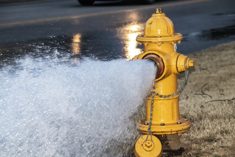 W górę żółtej pożarniczego hydranta podpływowej wody przez ulicę z mokrą autostradą i oponą od przelotnego samochodu za fotografia stock