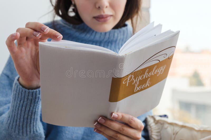 W górę dziewczyny czyta książkę na psychologii blisko okno w błękitnym pulowerze fotografia royalty free W górę dziewczyny czyta książkę na psychologii blisko okno w błękitnym pulowerze fotografia royalty free