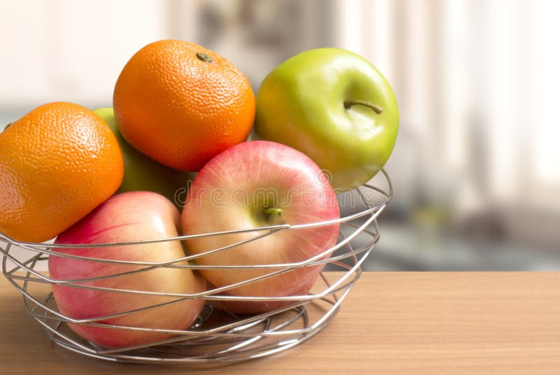 W górę owoc tak jak jabłka i pomarańcze w decoratively drucianym koszu stawiającym na kontuaru stole, kuchnia zamazywał tło obraz stock W górę owoc tak jak jabłka i pomarańcze w decoratively drucianym koszu stawiającym na kontuaru stole, kuchnia zamazywał tło obraz stock