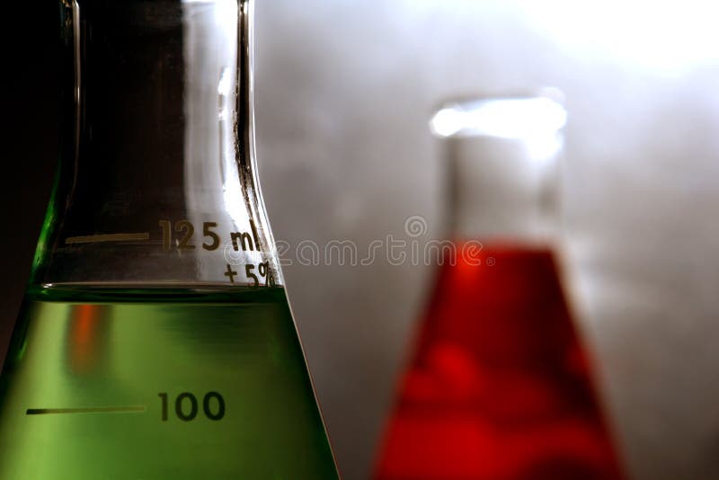 Laboratory glass conical Erlenmeyer flasks filled with green liquid and red chemical solution for a chemistry experiment in a science research lab. Laboratory glass conical Erlenmeyer flasks filled with green liquid and red chemical solution for a chemistry experiment in a science research lab