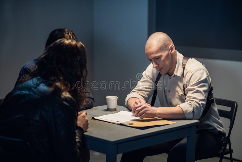 In the interrogation room, the investigator and the officer are talking to the criminal. In the interrogation room, the investigator and the officer are talking to the criminal.