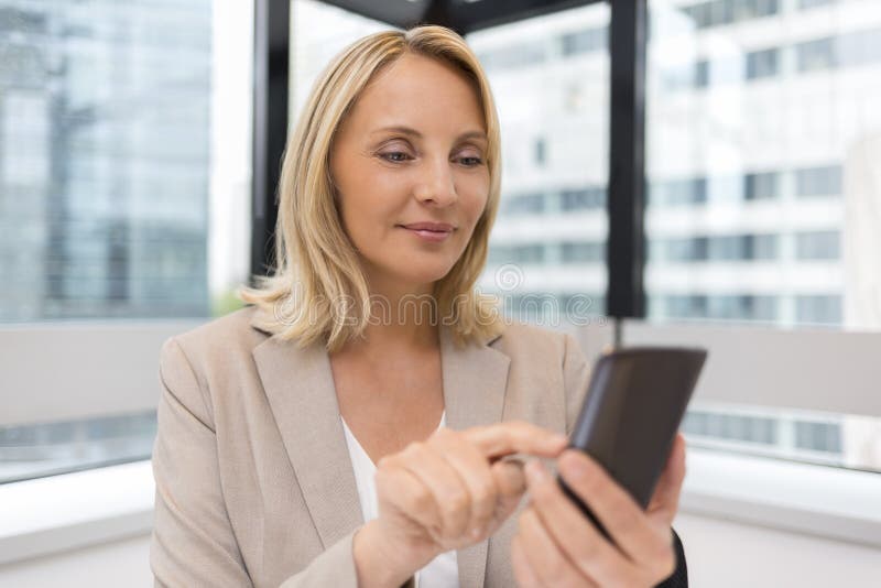 W średnim wieku biznesowa kobieta pracuje przy biurem Używać Smartphone obrazy stock W średnim wieku biznesowa kobieta pracuje przy biurem Używać Smartphone obrazy stock