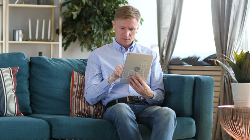 W Średnim Wieku mężczyzna Wyszukuje internet na pastylka pececie, Siedzi na leżance zbiory W Średnim Wieku mężczyzna Wyszukuje internet na pastylka pececie, Siedzi na leżance zbiory