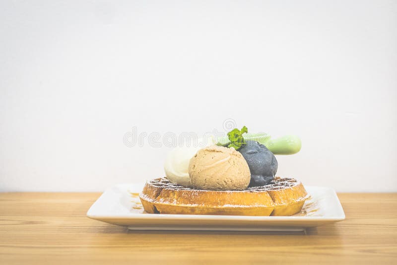 Waffle with Triple Scoop Ice-cream on top and served with maple syrup on white china plate royalty free stock image