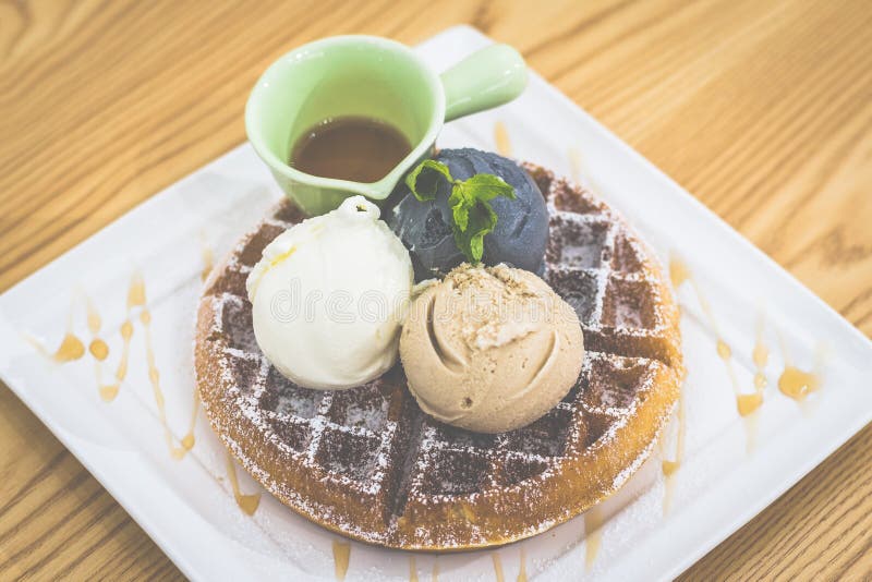 Waffle with Triple Scoop Ice-cream on top and served with maple syrup on white china plate stock photo