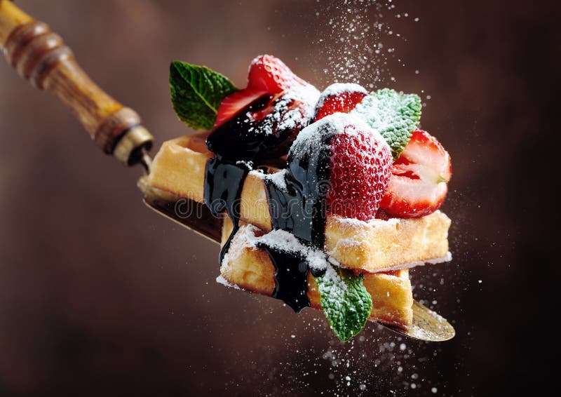 Waffles with strawberries, mint and chocolate sauce, sprinkled with powdered sugar