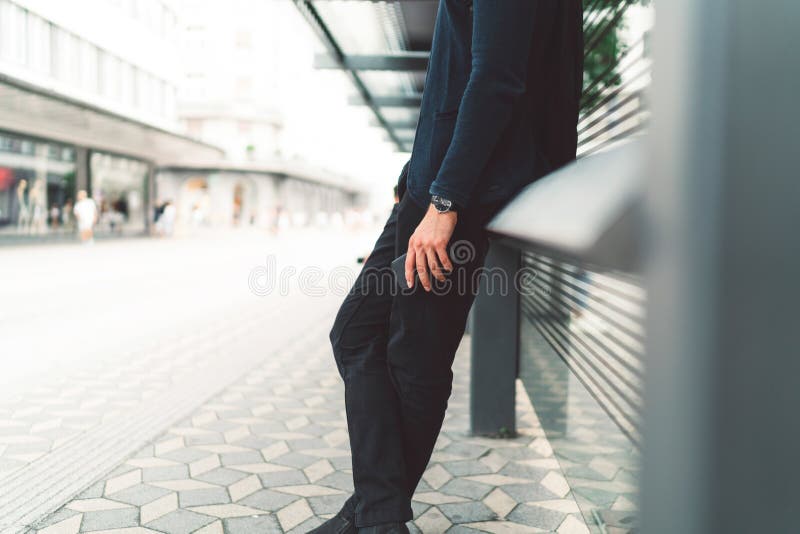 Waist down unrecognizable man in dark clothes on bright background waiting at the bus station stock image