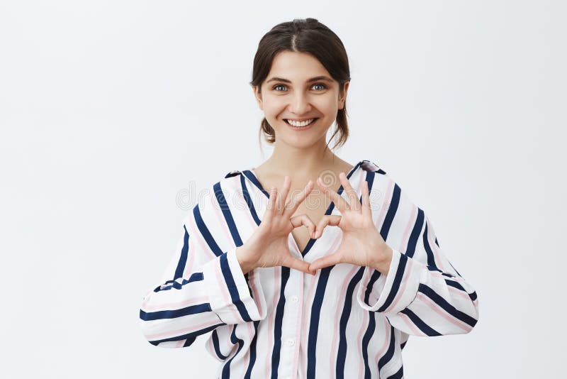 Waist-up shot of cute and feminine loving girlfriend in striped srtlish blouse showing heart sign over chest and smiling royalty free stock photos Waist-up shot of cute and feminine loving girlfriend in striped srtlish blouse showing heart sign over chest and smiling royalty free stock photos