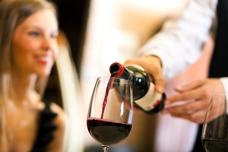 Cameriere serve il vino rosso per una bella donna in un ristorante.