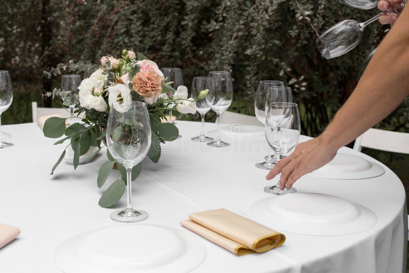 The waiter serves banquet table. Wedding table setting decorated with flowers and brass candlesticks with candles royalty free stock photography The waiter serves banquet table. Wedding table setting decorated with flowers and brass candlesticks with candles royalty free stock photography