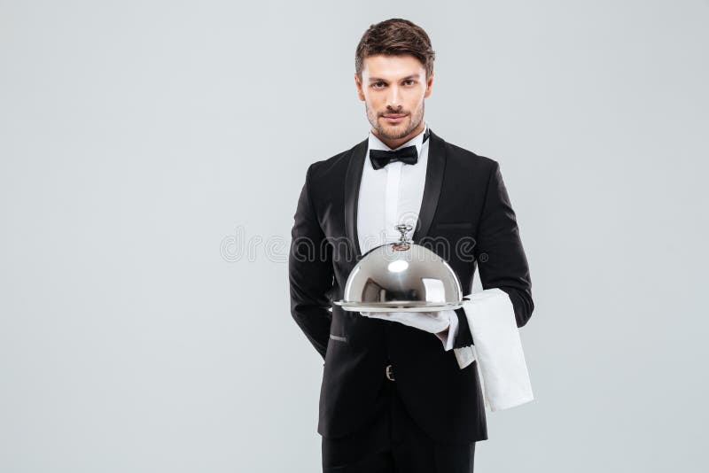 Waiter in tuxedo holding serving tray with cloche and napkin