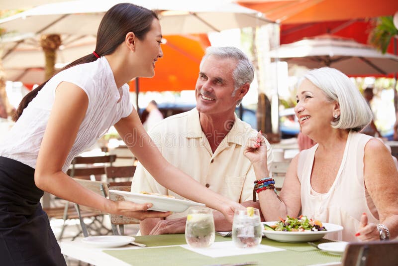 Waitress Serving Senior Couple Lunch In Outdoor Restaurant