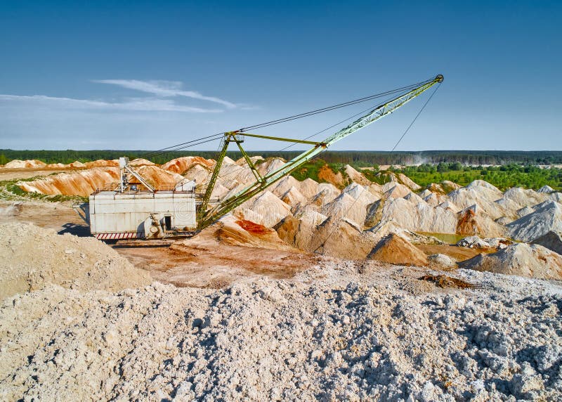 Walking dragline with hoist digs calx in chalkquarry on summer day. Old excavator mines limestone in large pit. Natural deposit extraction