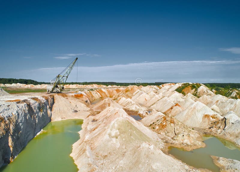 Walking dragline with hoist digs calx in chalkquarry on summer day. Old excavator mines limestone in large pit. Natural deposit extraction