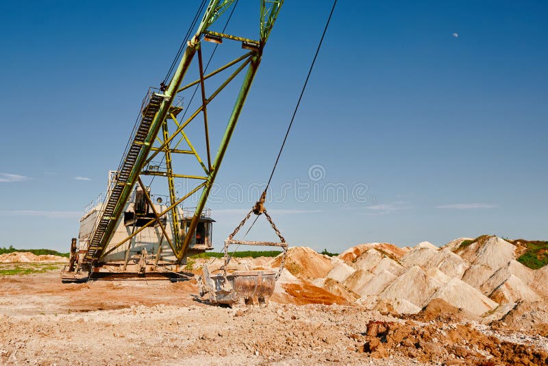 Walking excavator digs calx in chalk quarry on summer day. Big dragline operates in mining pit in countryside against clear blue sky